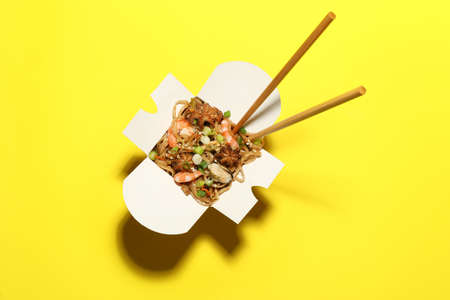 Box of noodle wok with chopsticks on yellow background, top view
