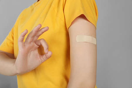 Vaccinated woman with medical plaster on her arm showing okay gesture against gray background, closeupの写真素材