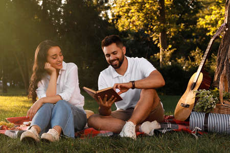 Happy young couple reading book on plaid in park. Summer picnicの写真素材