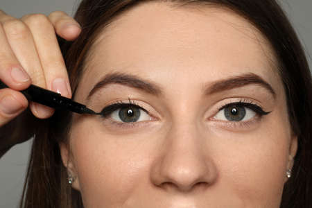 Artist applying black eyeliner onto woman's face on gray background, closeup