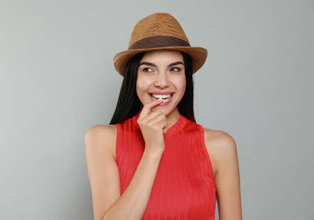 Beautiful young woman with straw hat on light gray background