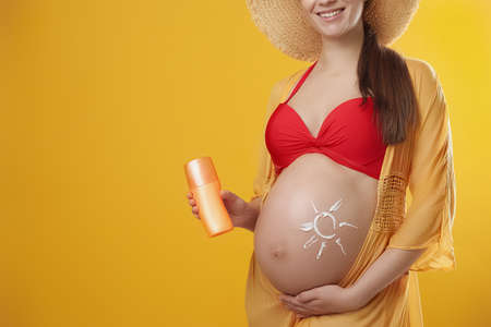 Young pregnant woman with sun protection spray on yellow background, closeup. Space for textの写真素材