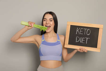 Happy woman holding celery and chalkboard with words Keto Diet on light gray backgroundの写真素材