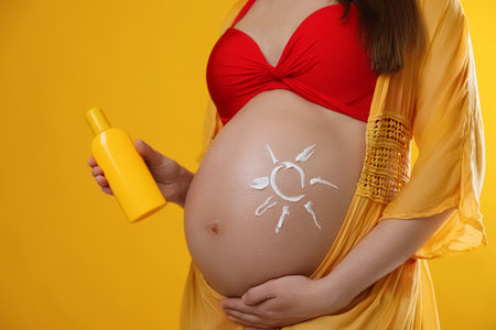 Young pregnant woman with sun protection cream on yellow background, closeupの写真素材