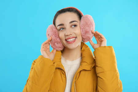 Beautiful young woman wearing earmuffs on light blue backgroundの写真素材