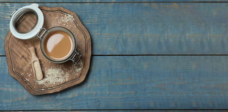 Jar of tasty sesame paste and seeds on light blue wooden table, top view. Space for text