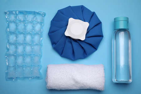 Bottle of water, cold compress, ice pack and towel on light blue background, flat lay. Heat stroke...