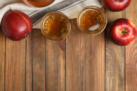 Delicious cider and ripe red apples on wooden table, flat lay. Space for textの写真素材