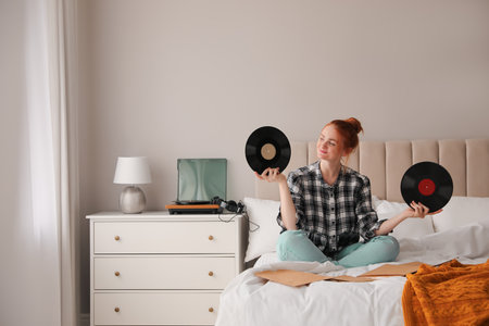 Young woman choosing vinyl disc to play music with turntable in bedroomの写真素材