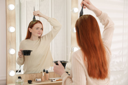 Young woman dyeing her hair with henna near mirrorの写真素材
