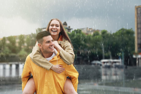 Lovely couple wearing raincoats under rain on city streetの写真素材