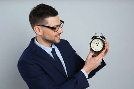 Happy businessman holding alarm clock on gray background. Time managementの写真素材
