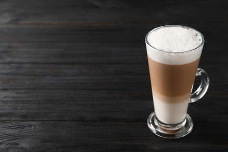 Glass cup of delicious layered coffee on black wooden table, space for textの写真素材