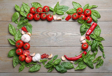 Frame made of fresh basil leaves and vegetables on wooden table, flat lay. Space for textの写真素材