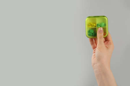 Woman holding plastic box with different pills on light gray background, closeup. Space for text