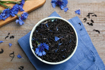 Bowl with dry tea leaves and cornflowers on wooden table, flat layの写真素材