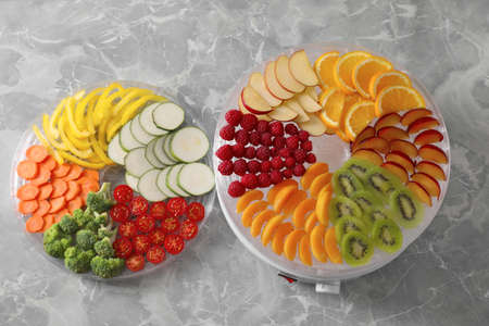 Cut fruits, vegetables and dehydrator machine on gray marble table, flat lay