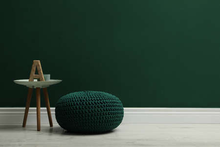 Stylish knitted pouf and table near green wall indoors, space for textの写真素材