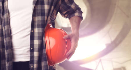Man with orange hard hat at construction site with unfinished building, closeup. Space for textの写真素材