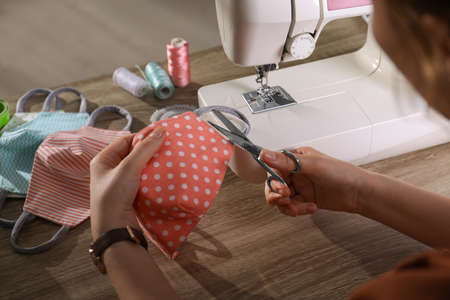 Woman sewing cloth protective mask with scissors and machine at table, closeupの写真素材