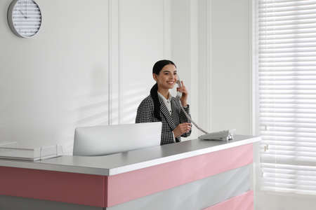 Receptionist talking on phone at countertop in officeの写真素材
