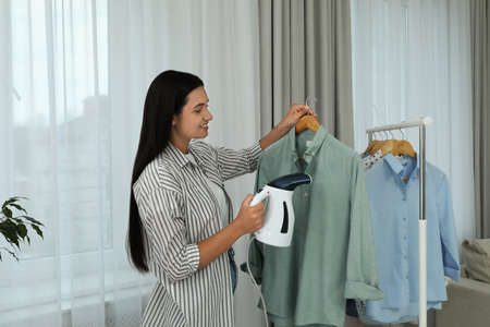 Woman steaming shirt on hanger at homeの写真素材