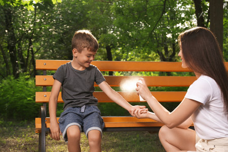 Woman applying insect repellent on her son's arm in park. Tick bites preventionの写真素材