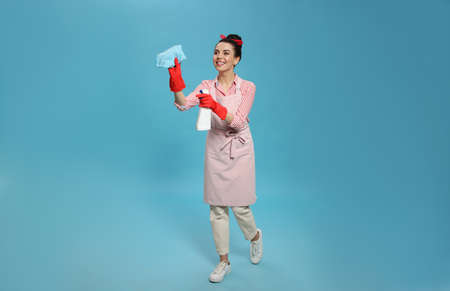 Young housewife with detergent and rug on light blue backgroundの写真素材
