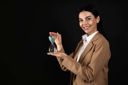 Businesswoman holding hourglass on black background, space for text. Time management