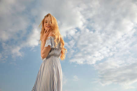 Beautiful young woman against blue sky on sunny day, space for textの写真素材