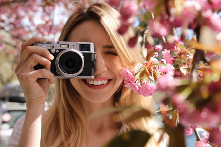 Happy female tourist taking photo of blossoming sakura outdoors on spring day