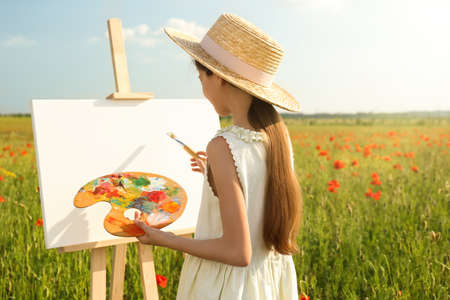 Little girl painting on easel in beautiful poppy fieldの写真素材