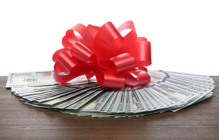 Dollar bills with red bow on wooden table against white background