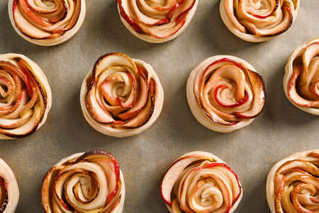 Freshly baked apple roses on parchment paper, flat lay. Beautiful dessertの写真素材