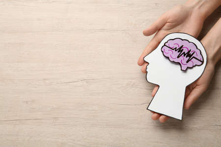 Woman holding human head and brain cutouts at wooden table, top view with space for text. Epilepsy...