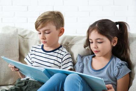 Little boy and girl reading book on sofa at homeの写真素材