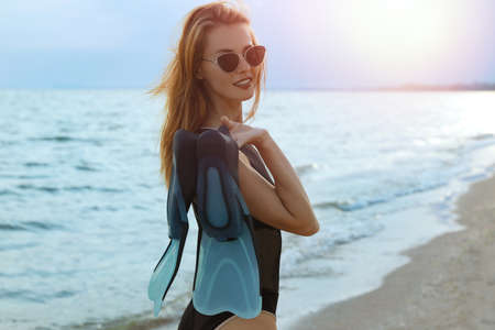 Happy woman with flippers near sea on beach