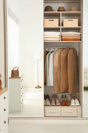 Garment bags with clothes on rack in wardrobe indoorsの写真素材
