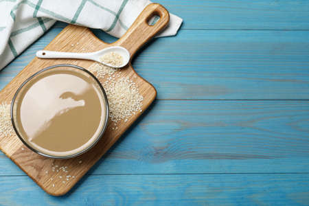 Tasty sesame paste, seeds and spoon on light blue wooden table, top view. Space for text