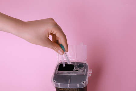 Woman throwing used syringe needles into sharps container on pink background, closeup