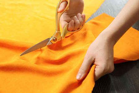 Seamstress cutting orange fabric with scissors at workplace, closeupの写真素材
