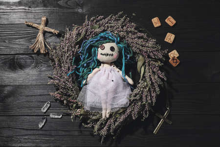 Female voodoo doll with pins surrounded by ceremonial items on black wooden background, flat layの写真素材