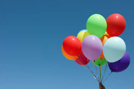 Woman with bunch of colorful balloons against blue sky. Space for textの写真素材