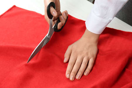 Seamstress cutting red fabric with scissors at workplace, closeupの写真素材