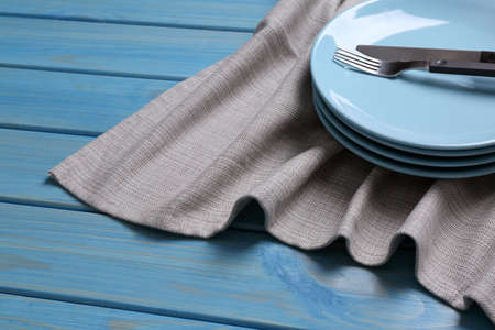 Clean kitchen towel and stack of plates with cutlery on blue wooden table