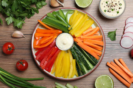 Fresh raw vegetable sticks and sauce on wooden table, flat lay