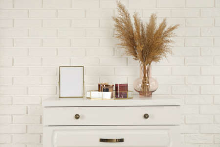 Modern chest of drawers with decor near white brick wall