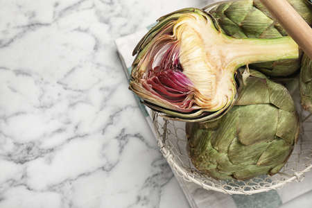 Cut and whole fresh raw artichokes on white marble table, top view. Space for textの写真素材