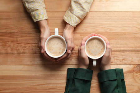 Women with cups of coffee at wooden table, top viewの写真素材