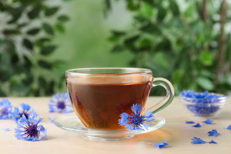 Glass cup of tea and cornflowers on wooden tableの写真素材